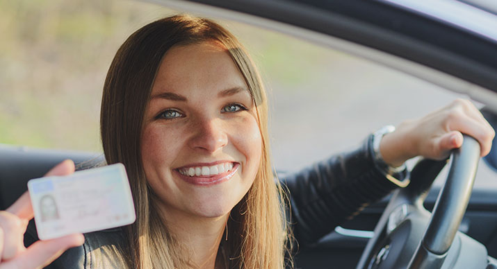 Young lady holding her new driver license in a car